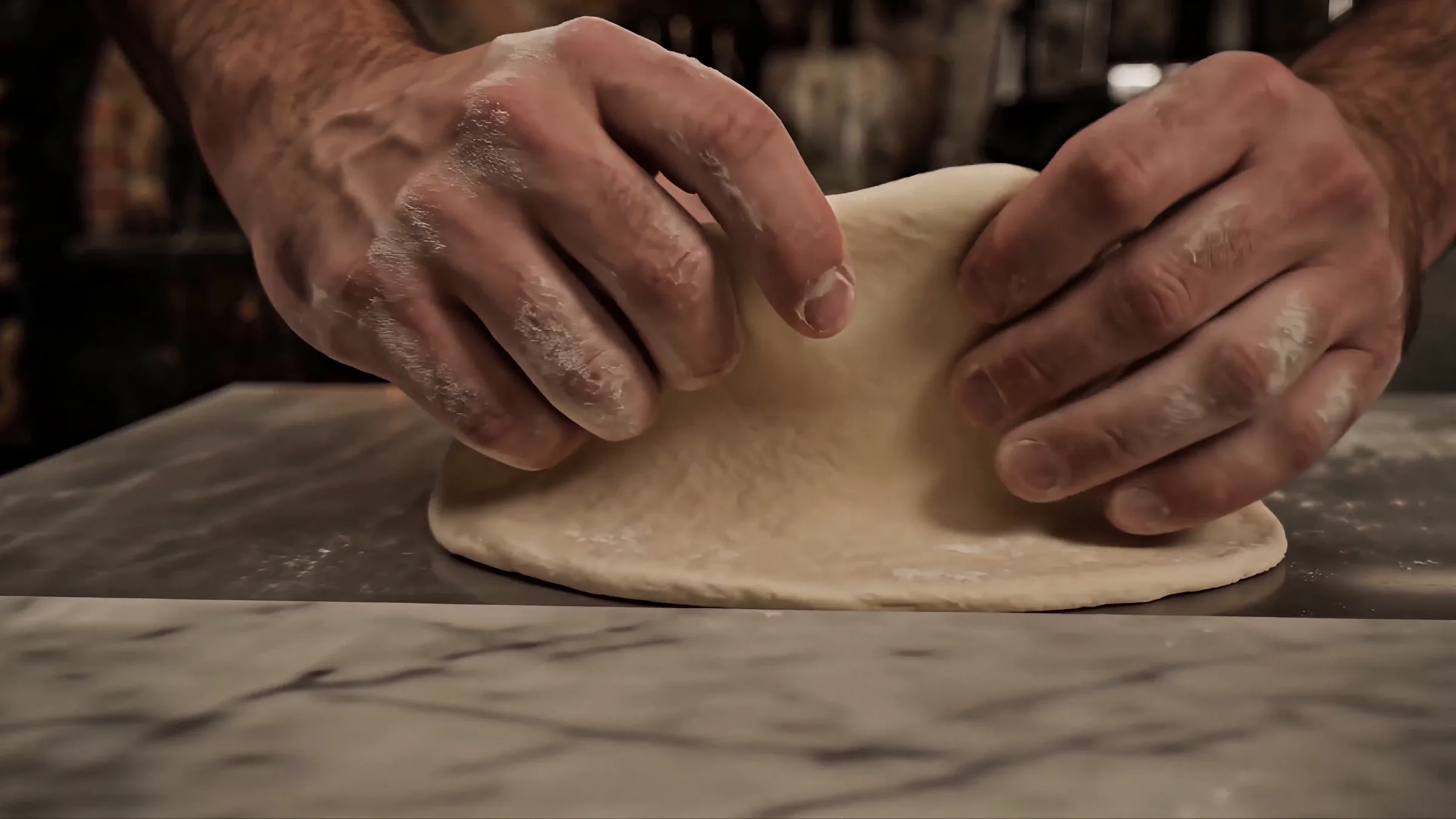 Deux mains étirent une boule de pâte sur un plan de travail en marbre
